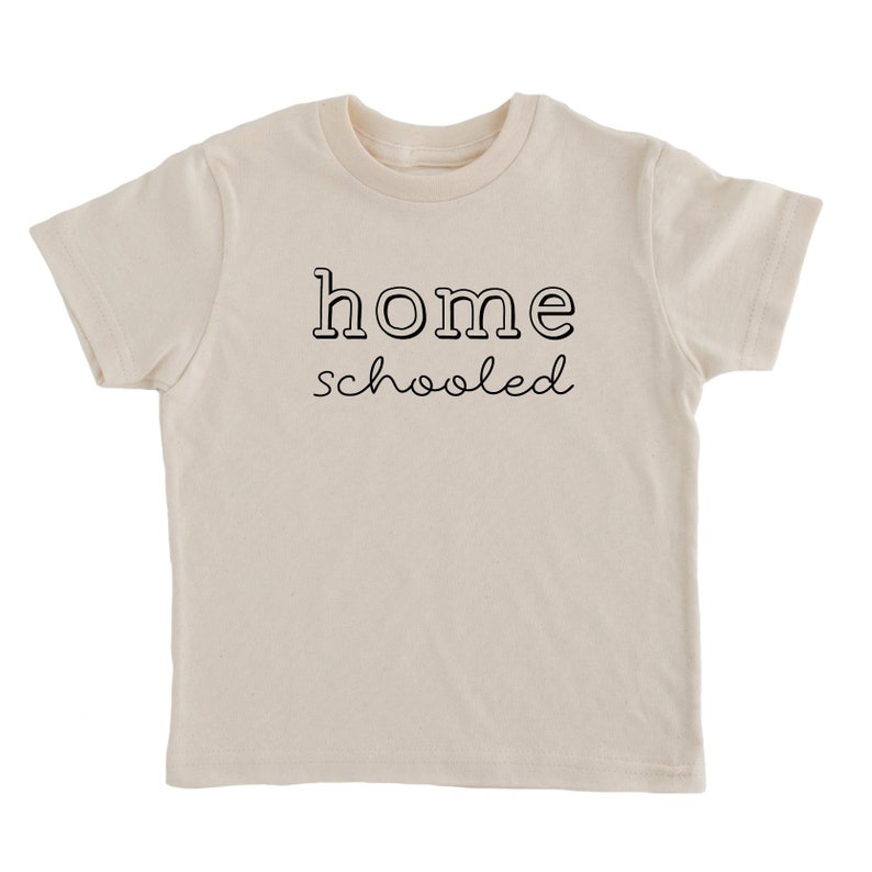 May include: A cream colored t-shirt with the text "home schooled" printed in black.