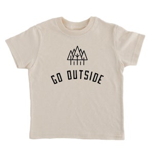 May include: A cream-colored short-sleeved t-shirt with a black graphic of a mountain range and trees. The text "GO OUTSIDE" is printed below the graphic.