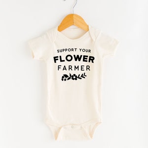 May include: A cream-colored baby onesie with short sleeves and black text that reads "Support Your Flower Farmer" with a small flower graphic below the text.