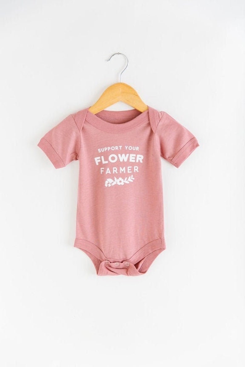 May include: A pink baby onesie with short sleeves and a white graphic that says "Support Your Flower Farmer".
