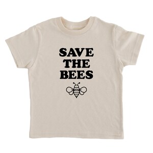 Puede incluir: Una camiseta de color crema con texto negro que dice "SAVE THE BEES" y una ilustraci&oacute;n de abeja negra.