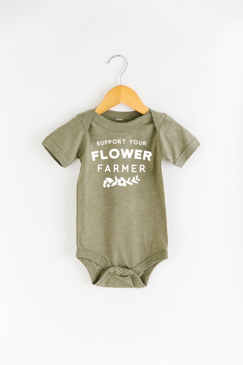 May include: A green baby onesie with white text that reads "Support Your Flower Farmer" with a small floral design below the text.