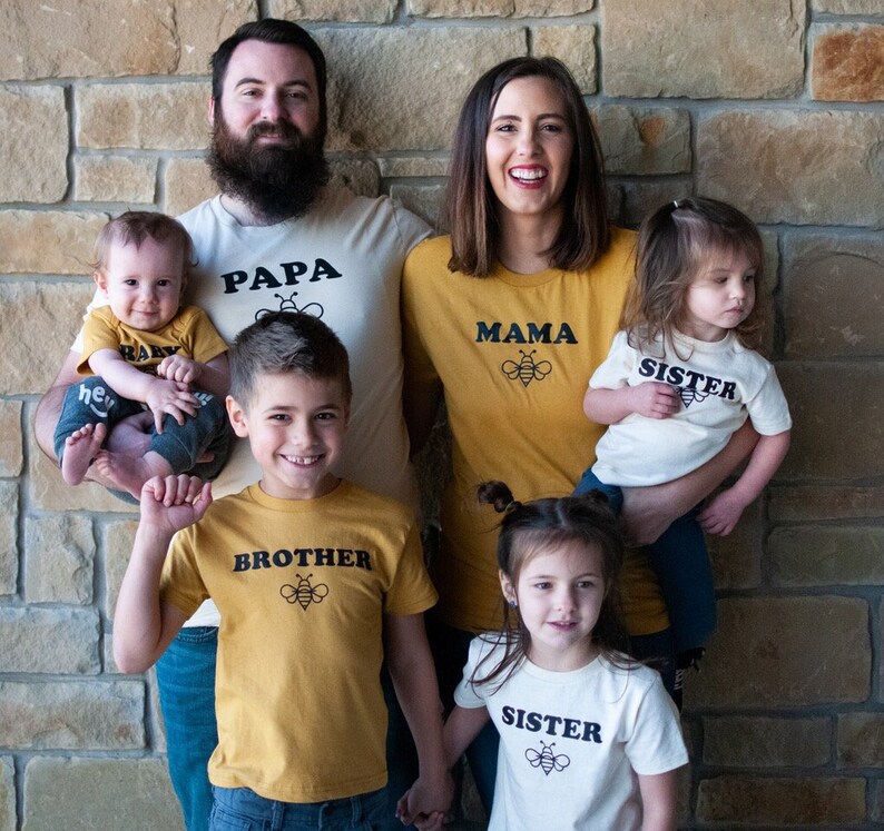 May include: A family of five wearing matching shirts with bee designs. The shirts say "Papa", "Mama", "Brother", "Sister", and "Baby".
