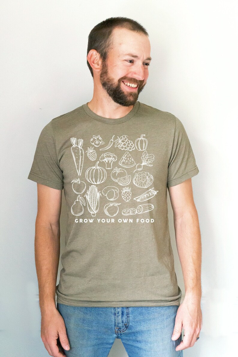 May include: A man wearing a green t-shirt with a white graphic of various fruits and vegetables. The text "GROW YOUR OWN FOOD" is printed below the graphic.