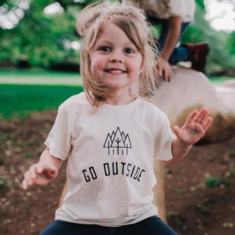 May include: A white t-shirt with a black graphic of a mountain range and trees. The text "GO OUTSIDE" is printed below the graphic.