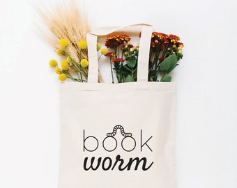 May include: A white tote bag with black text that reads "book worm" and a small worm illustration above the word "book". The bag is filled with a bouquet of yellow and red flowers.