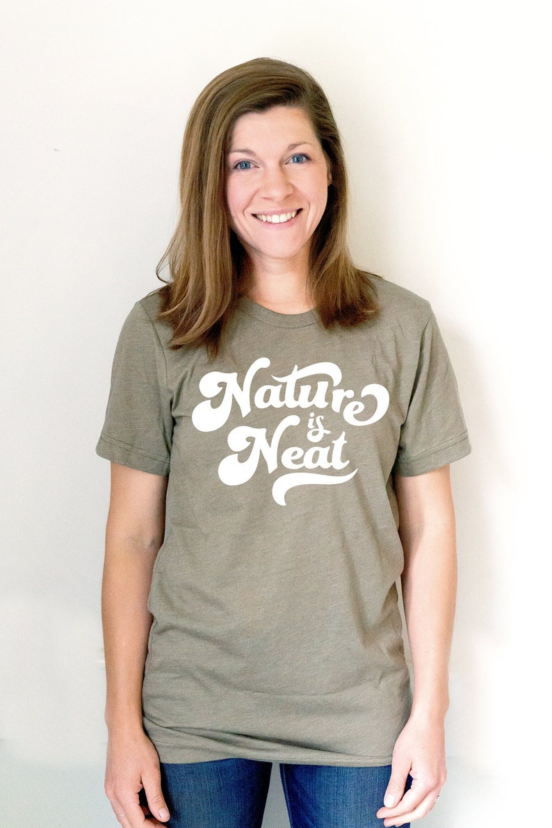 May include: A woman wearing a green t-shirt with the text "Nature is Neat" in white lettering. The shirt has a relaxed fit and short sleeves.