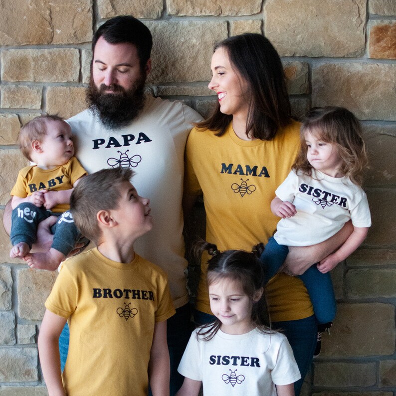 K&ouml;nnte beinhalten: Eine f&uuml;nfk&ouml;pfige Familie tr&auml;gt passende T-Shirts mit Bienenmotiven. Die Shirts sagen "Papa", "Mama", "Baby", "Bruder" und "Schwester".