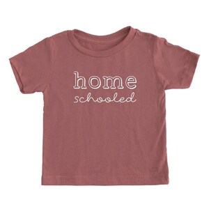 May include: A maroon short-sleeved t-shirt with the text "home schooled" in white.