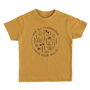 Puede incluir: Una camiseta de color amarillo mostaza con un dise&ntilde;o gr&aacute;fico negro en forma de c&iacute;rculo con el texto "Not all classrooms have four walls" y varios iconos de exteriores.