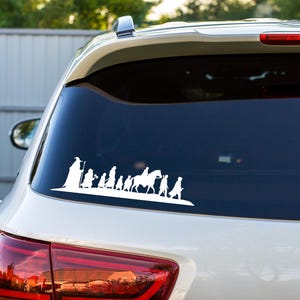 May include: White vinyl decal showing a silhouette of a group of figures, including a wizard, riders on horseback, and other characters, likely from a fantasy story. The decal is applied to the rear window of a white car.