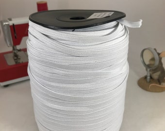 May include: A spool of white elastic cord wound around a black plastic spool. The elastic cord is used for sewing and crafting projects.