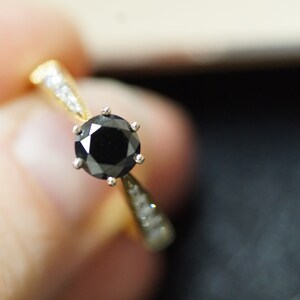 May include: A gold ring with a black diamond centre stone and smaller diamonds on the band.