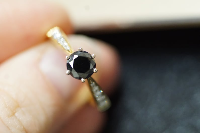 May include: A gold ring with a black diamond centre stone and smaller diamonds on the band.