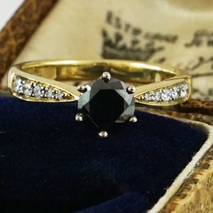 May include: A gold engagement ring featuring a black diamond centre stone and a band of small diamonds.