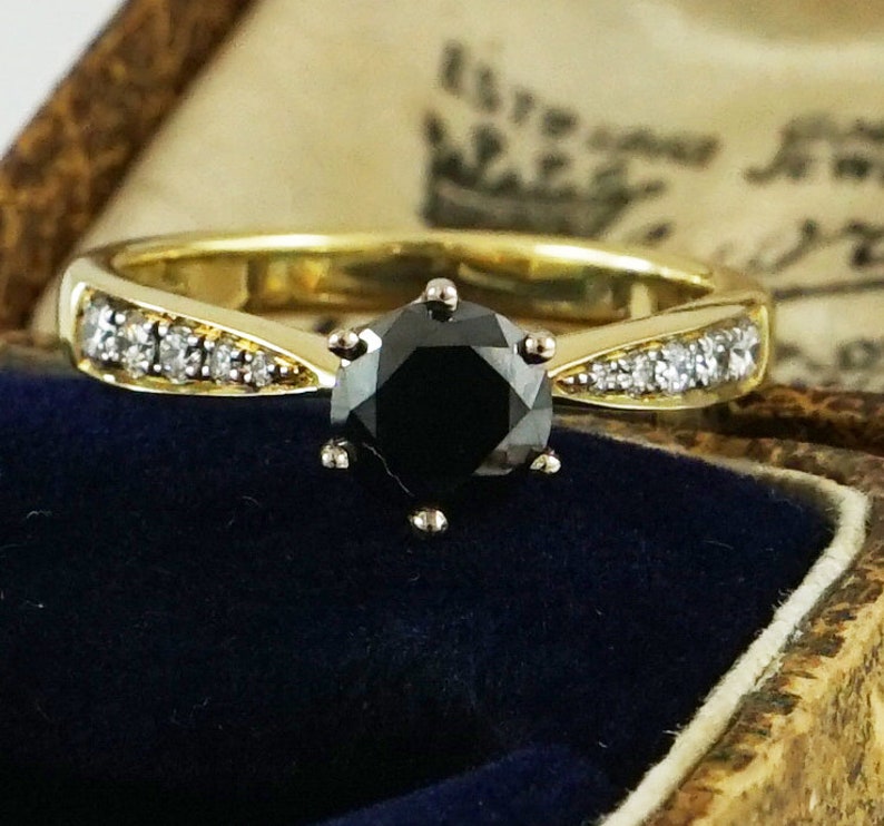 May include: A gold engagement ring featuring a black diamond centre stone and a band of small diamonds.