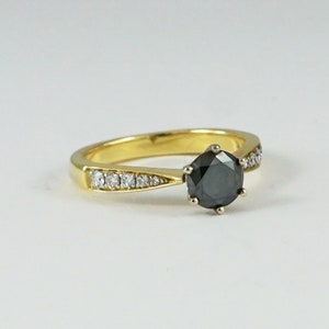May include: A gold ring featuring a black diamond centre stone and a band of smaller diamonds.