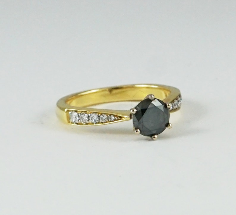 May include: A gold ring featuring a black diamond centre stone and a band of smaller diamonds.