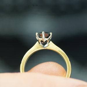 May include: A gold ring with a black gemstone set in a white metal prong setting.