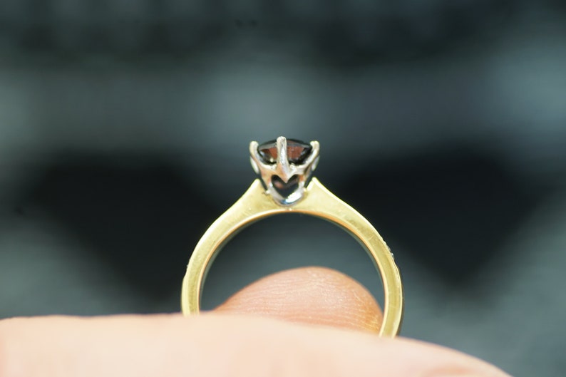 May include: A gold ring with a black gemstone set in a white metal prong setting.