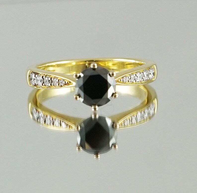 May include: A gold ring featuring a black diamond centre stone and smaller diamonds set in the band.