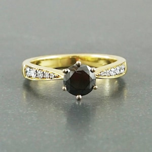 May include: A gold engagement ring featuring a black diamond centre stone and a band of smaller diamonds.