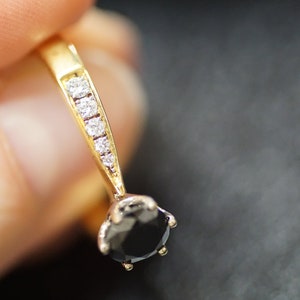 May include: A gold ring featuring a black gemstone and a line of small clear gemstones.