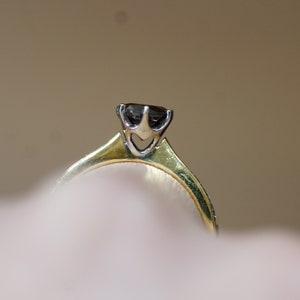 May include: A gold ring with a black diamond set in a prong setting.