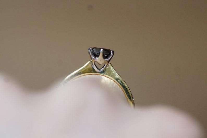 May include: A gold ring with a black diamond set in a prong setting.
