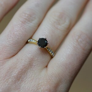 May include: A gold ring featuring a black gemstone surrounded by smaller white gemstones.