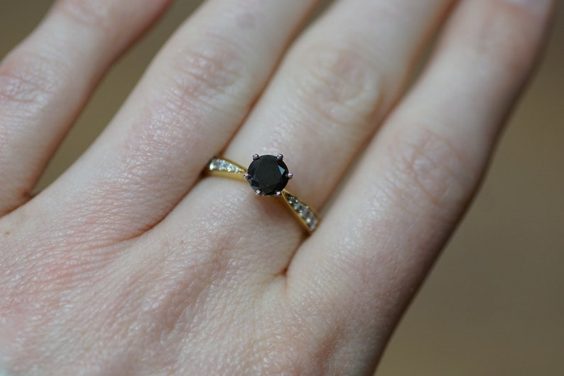 May include: A gold ring featuring a black gemstone surrounded by smaller white gemstones.