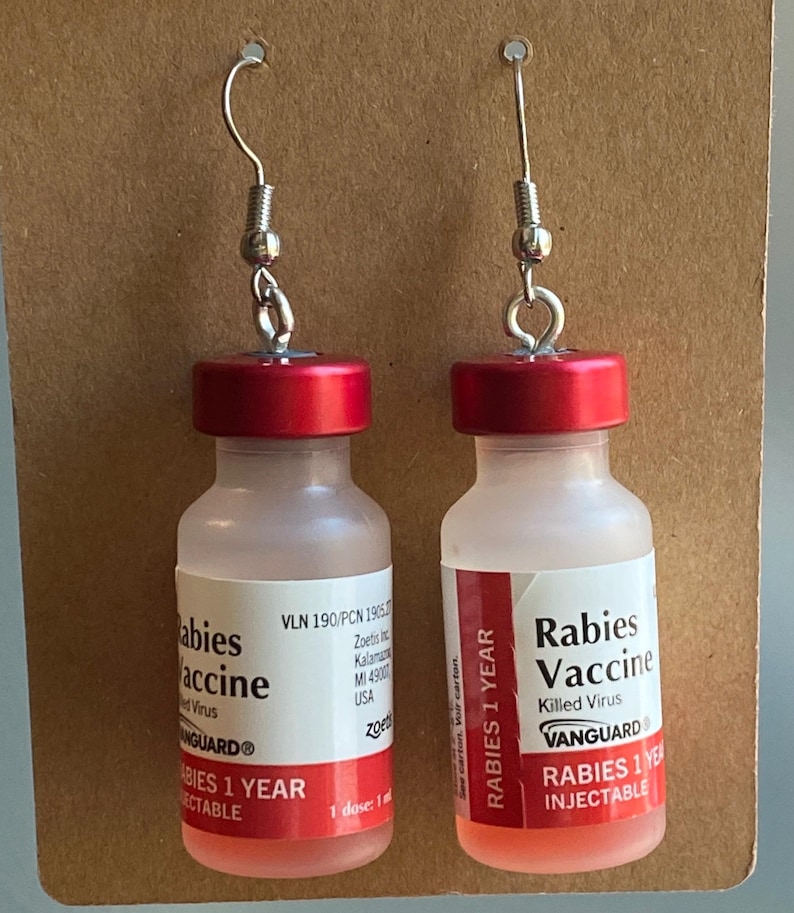 May include: A pair of red and clear glass vial earrings with silver hooks. The vials are labeled "Rabies Vaccine" and "Babies Vaccine" with the text "Rabies 1 Year Injectable" and "Babies 1 Year Injectable".