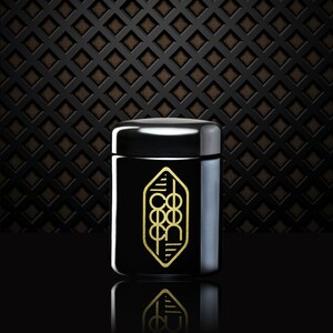 Pode incluir: Um frasco preto com um design geométrico dourado e a palavra "COEXIST" dentro do design. O frasco está sobre uma superfície preta.
