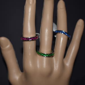 Può includere: Tre anelli d'argento con pietre preziose colorate. Gli anelli sono su un manichino di mano. Gli anelli hanno pietre preziose rosa, verdi e blu.