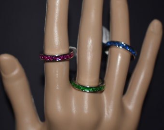 Puede incluir: Tres anillos de plata con piedras preciosas de colores. Los anillos están en un maniquí de mano. Los anillos tienen piedras preciosas rosas, verdes y azules.