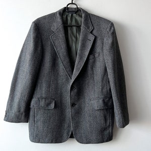 Puede incluir: Una chaqueta gris de espiga con cierre de dos botones y dos bolsillos delanteros.