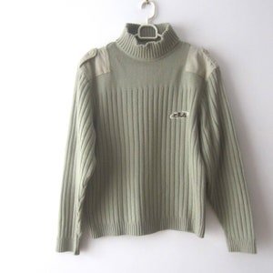 May include: A green ribbed turtleneck sweater with a patch on each shoulder and the word "FILA" embroidered on the front.