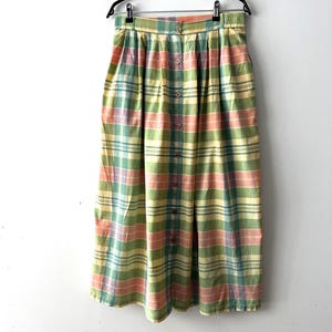 May include: A long, green, pink and yellow plaid skirt with a button front closure. The skirt is pleated and has a high waist.