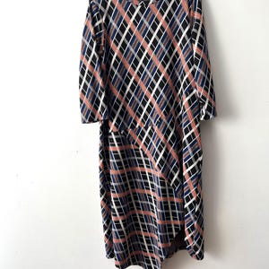 Op de afbeelding: Een zwarte, blauwe en roze geruite jurk met lange mouwen en een asymmetrische zoom.