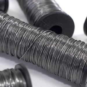 Può includere: Primo piano di diverse bobine di filo grigio. Ogni bobina ha un'anima in plastica nera. Il filo è avvolto strettamente attorno all'anima. Le bobine sono disposte in un primo piano, alcune a fuoco e altre sfocate.