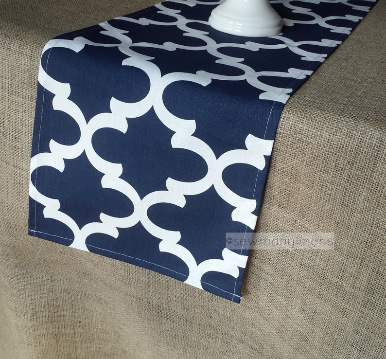 May include: A navy blue table runner with a white geometric pattern. The runner is made of fabric and has a subtle sheen.