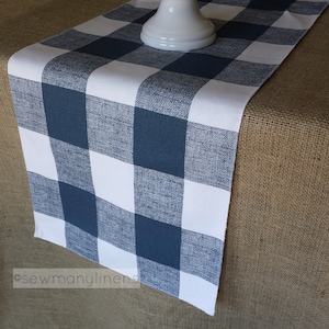 May include: A navy blue and white checked table runner. The runner is made of a woven fabric and has a slightly textured surface.