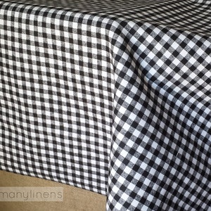 May include: Black and white gingham tablecloth with a small check pattern. The tablecloth is folded and draped over a table.