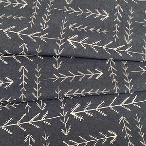 May include: Dark blue fabric with a repeating pattern of white, stylized tree branch designs. The fabric is folded, showing the texture and the arrangement of the pattern. The design is simple and modern.