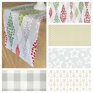 May include: A gray table runner with a pattern of red, green, and white dotted tree shapes. Additional fabric swatches show various patterns, including stars, arrows, and a buffalo check design. The runner is displayed on a burlap surface.