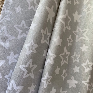 Puede incluir: Una toalla de cocina de tela gris con un patrón de estrellas blancas. La toalla está doblada en tres partes y las estrellas están pintadas a mano.