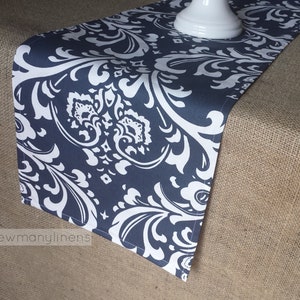 May include: A navy blue table runner with a white damask pattern. The runner is lying on a hessian surface.