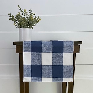 May include: A blue and white checkered table runner on a wooden table. The runner is made of a woven fabric and has a farmhouse style.