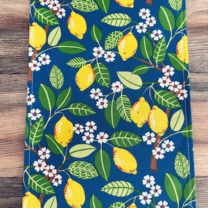 May include: A rectangular fabric item with a vibrant pattern of yellow lemons, green leaves, and white flowers on a deep blue background. The design resembles a lemon tree, creating a fresh and summery aesthetic.