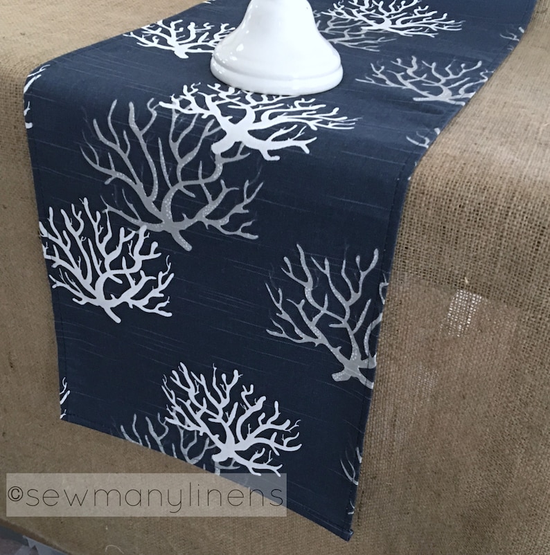 May include: A navy blue table runner with a white coral design. The runner is on a hessian surface.